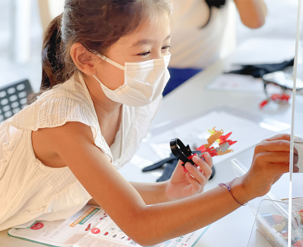 画像：第６の指の機械を手に取り、新しいパーツを加えようとしている女の子の様子