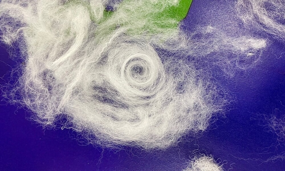 日本列島を模した地図の上に、わたで作られた台風の渦巻き状の雲が表現されている。
