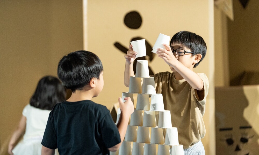 2人の子どもが協力して紙コップを高く積み上げている様子。