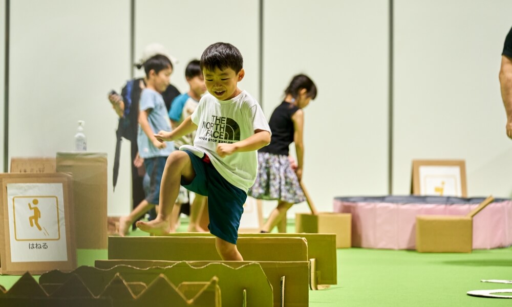 段ボールで作られたアスレチックコースで飛び跳ねながら遊ぶ男の子の様子。