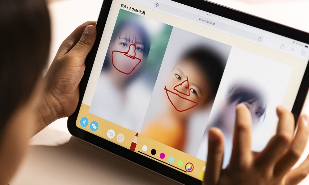 子どもがタブレットを使い、顔写真に目や鼻を描き込むアプリを操作している様子。