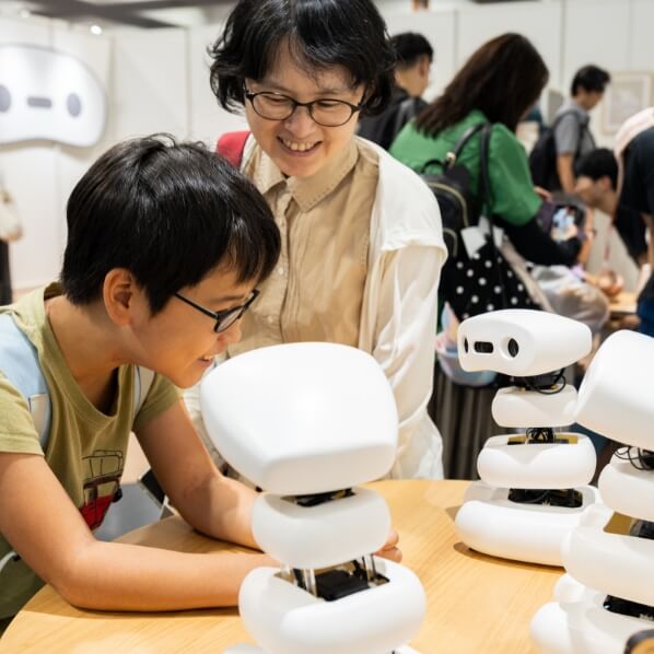 子どもと大人が展示されている白い小型ロボットを一緒に覗き込んでいる様子。