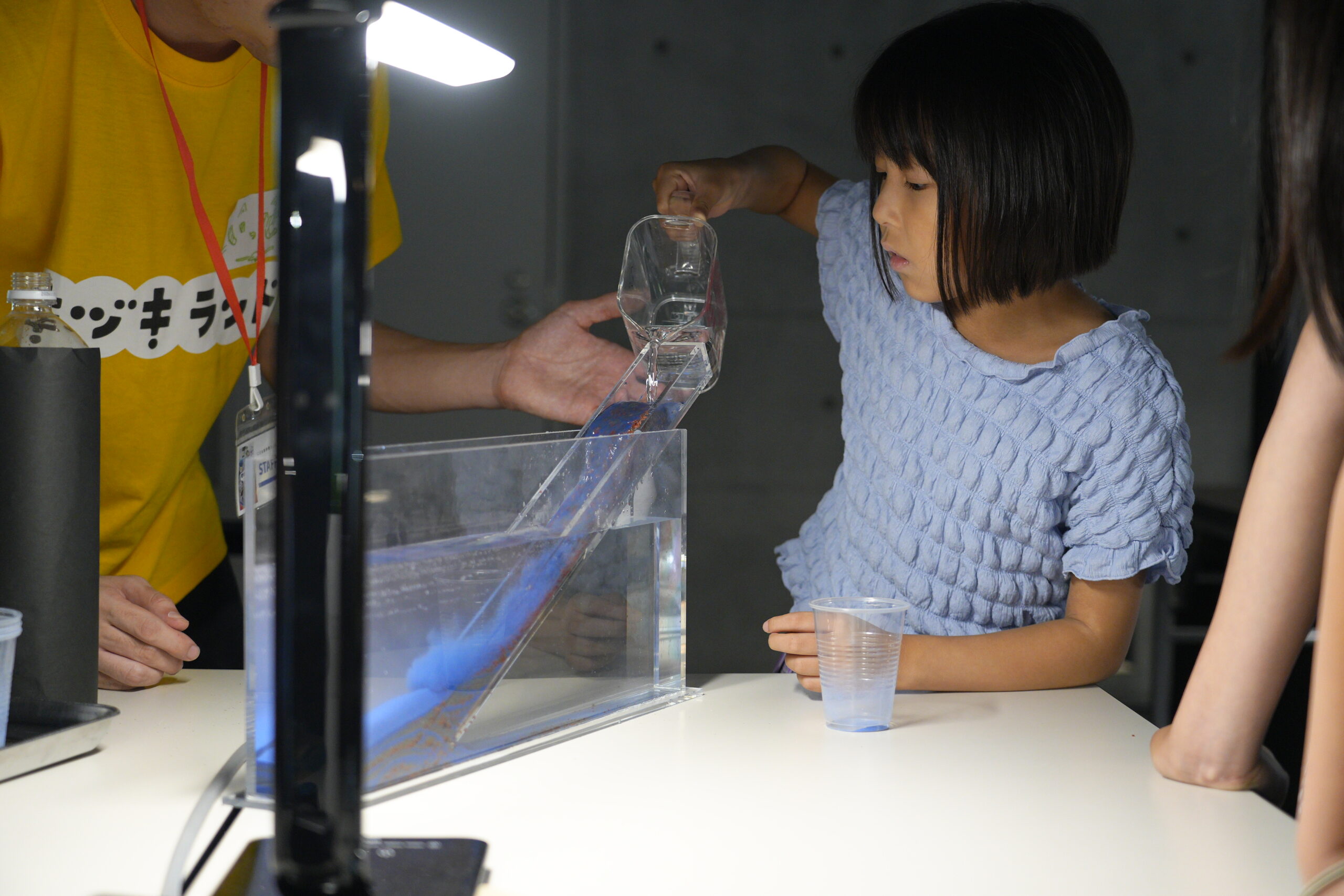 水と、粒の大きさで色分けされた砂を水槽に入れて地層が積み重なる様子を観察する子ども